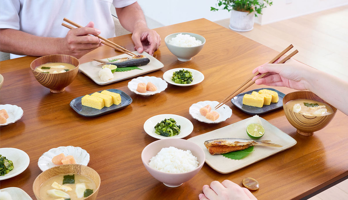 ヘーベルハウス横浜展示場 区画19のダイニングで夫婦がごはんを食べる様子 テーブルにはやまやコミュニケーションズのあご明太、高菜や明太子が並ぶ